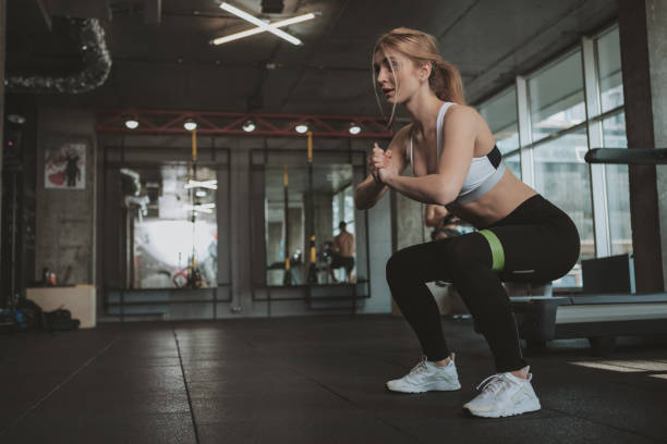 Fit woman performing resistance band squats in a modern gym for functional strength training.