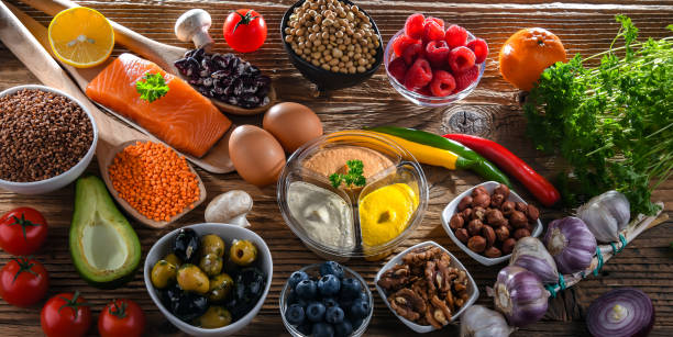 A variety of healthy foods rich in nutrients, including salmon, legumes, nuts, fruits, and vegetables, displayed on a wooden table for balanced nutrition.