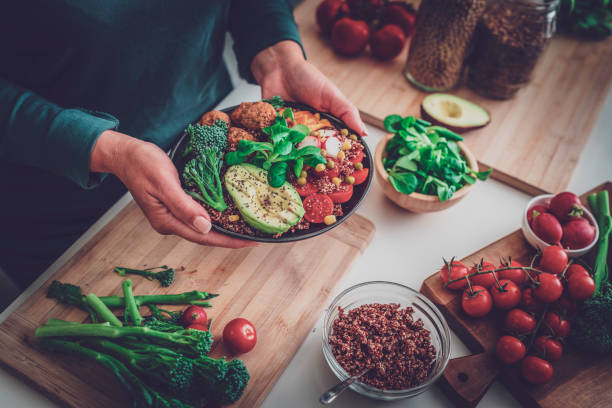 A person holding a colorful plant-based meal with fresh vegetables, quinoa, and avocado, promoting healthy eating and a plant-based diet.