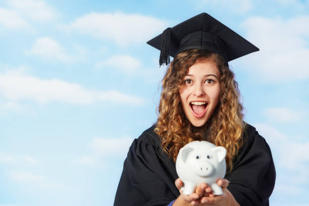 A graduate in a cap and gown holding a piggy bank, symbolizing student loan and debt management.