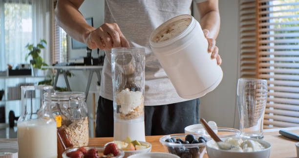 A person preparing a protein smoothie with various healthy ingredients, highlighting the importance of sports nutrition and post-workout recovery meals.