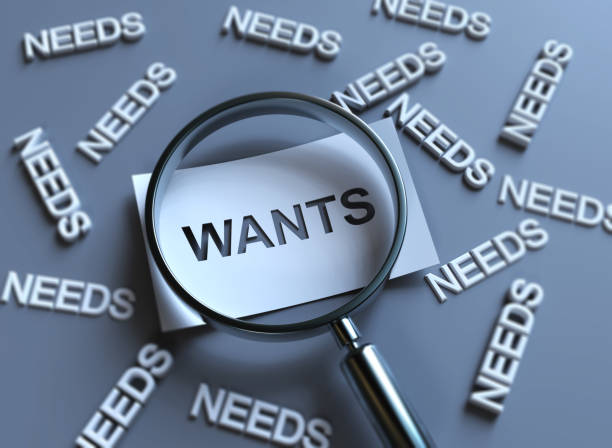 A magnifying glass focusing on the word "Wants" while surrounded by multiple "Needs," symbolizing the challenge of prioritizing financial decisions.