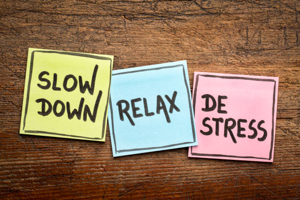 Three colorful sticky notes on a wooden surface displaying handwritten words: "Slow Down," "Relax," and "De-Stress," emphasizing the importance of relaxation and stress relief.