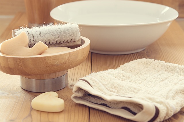 A wooden bowl with a brush, soap bars, and a soft towel placed near a washbasin.