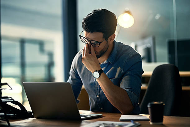 Stressed businessman rubbing his eyes while working late on a laptop, showing the effect of stress on mental fatigue and productivity.