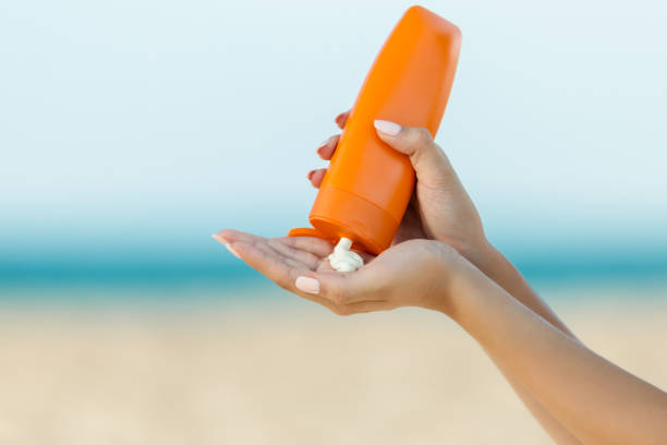 A close-up of a person dispensing lightweight moisturizer from an orange bottle onto their palm at the beach, highlighting summer skincare and hydration.