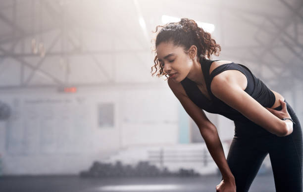 A focused woman in workout attire catching her breath in a gym, representing the drive to stay motivated, work out, and exercise consistently.