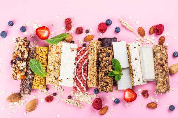 A variety of high-protein snack bars with nuts, berries, and oats on a pink background, showcasing nutritious options for athletes and active individuals.