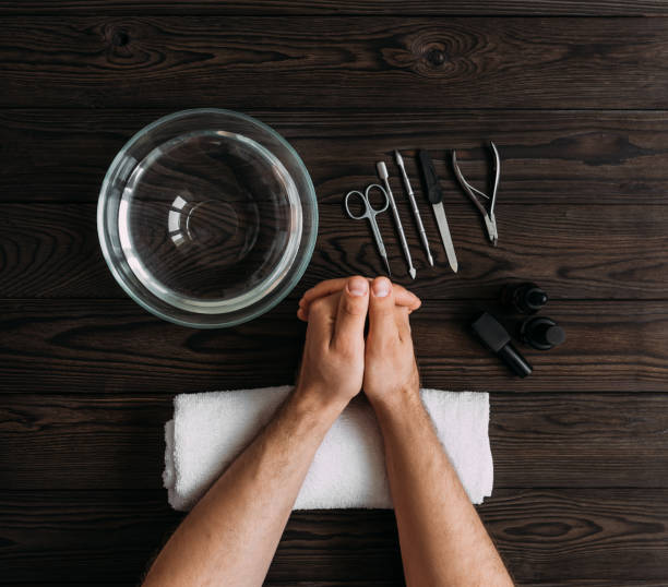 A pair of hands resting on a towel beside nail care tools, a bowl of water, and essential oils, representing steps to keep your nails clean and healthy.