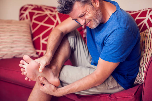 Man sitting on a couch, holding his foot in pain.