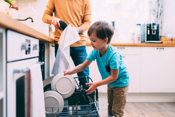 A young boy helping unload the dishwasher, demonstrating how to teach kids proper hygiene habits through daily chores in the kitchen.