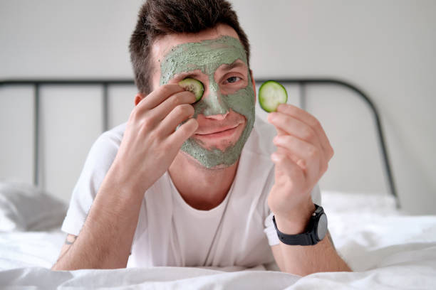 A man applying a natural face masks with cucumber slices, promoting glowing skin and organic skincare.