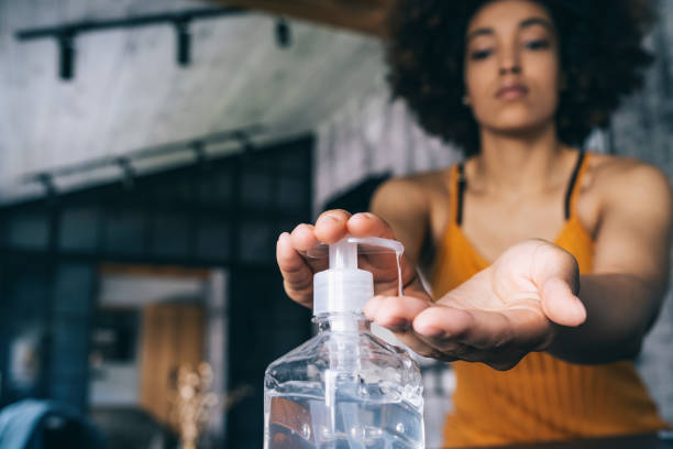 A woman applying hand sanitizer, dispensing it from a clear bottle into her palm while focusing on hygiene in a modern indoor setting.