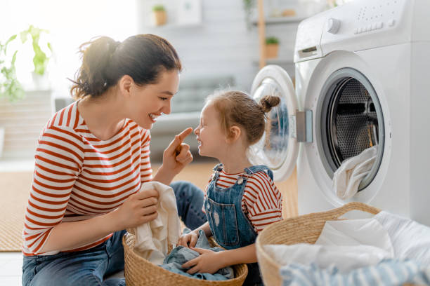 A mother and her young daughter smiling while doing laundry together, teaching kids proper hygiene habits through daily household chores.