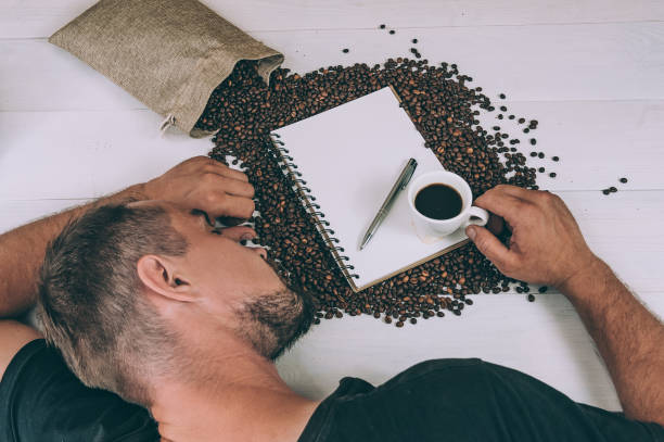 Man sleeping on coffee beans with a notebook and cup of coffee, illustrating how caffeine affects anxiety and sleep quality by disrupting rest and increasing alertness.