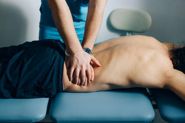 A chiropractor performing spinal adjustment therapy on a patient lying face down on a treatment table, focusing on chiropractic care in pain management.