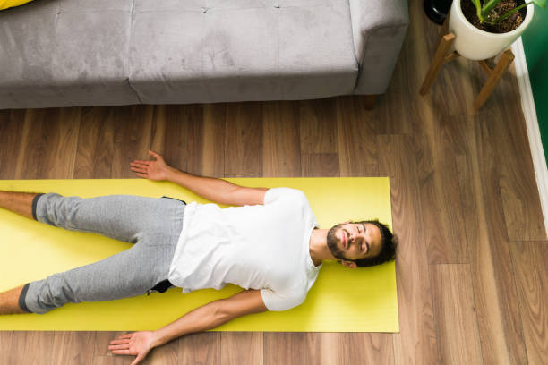 A man in Savasana yoga pose lying on his back on a mat, arms resting by his sides, providing deep relaxation and pain relief.