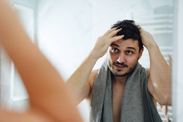 Man applying hair conditioner while looking in the mirror.