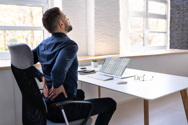 Man experiencing back pain while sitting at a desk due to poor posture.