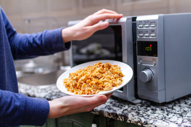 Person placing a plate of food into a microwave for heating.