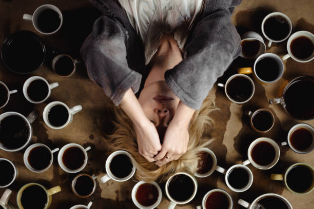 A stressed woman lying on a table surrounded by coffee cups, illustrating how caffeine affects anxiety and sleep quality.