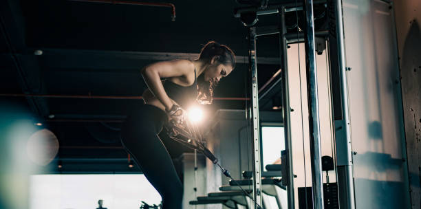 Woman performing weightlifting exercise using a cable machine in a gym.