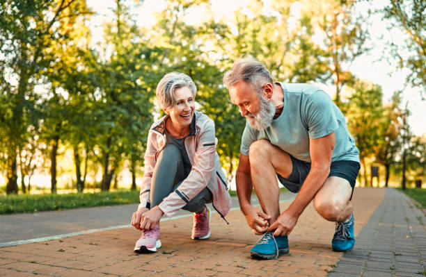 Elderly couple tying their sneakers in a park, preparing for a workout session to stay fit and active.