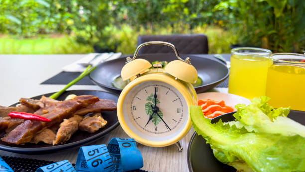 A dining table with healthy food, a clock, and a measuring tape, symbolizing the benefits of intermittent fasting to naturally improve insulin sensitivity.