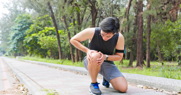 A male runner kneeling on a paved path, holding his knee in discomfort, highlighting the need to manage arthritis pain naturally.