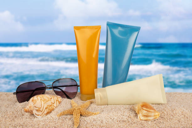 Lightweight moisturizers in summer-themed bottles with sunglasses and seashells on a sandy beach, with ocean waves in the background.