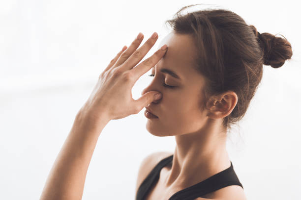 A young woman practicing deep breathing exercises with one hand on her nose, demonstrating a technique to alleviate pain and promote relaxation.