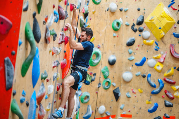 Man climbing an indoor rock wall using colorful handholds, demonstrating strong grip strength.