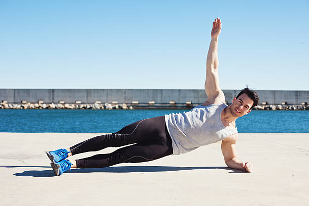 A man in athletic wear holding a side plank position outdoors, building core endurance and stability.