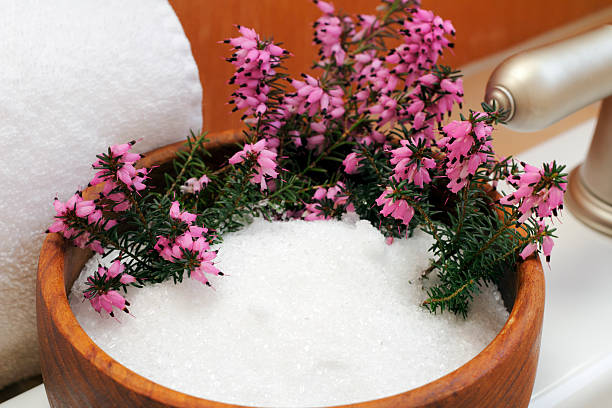 A wooden bowl filled with Epsom salt and fresh pink flowers, symbolizing a relaxing Epsom Salt Baths for Muscle Recovery.
