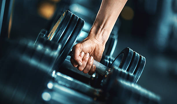 Hand gripping a heavy dumbbell in a gym, emphasizing grip strength and forearm engagement.