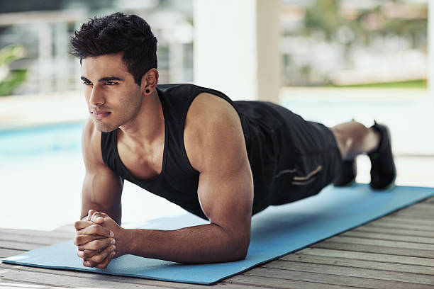A fit man performing a forearm plank on a yoga mat, engaging his core muscles for stability and strength.