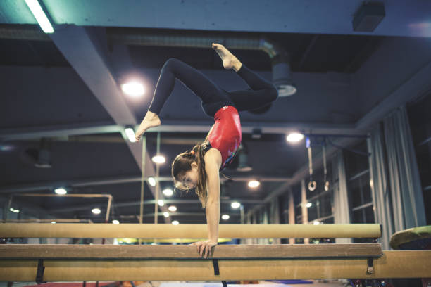 A skilled gymnast performing a handstand on a balance beam, showcasing strength, flexibility, and control to improve your stamina and endurance in gymnastics.