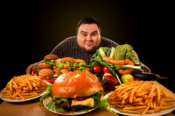 A man looking intensely at a table filled with fast food and fresh vegetables, symbolizing the debate on dietary fat and weight gain.